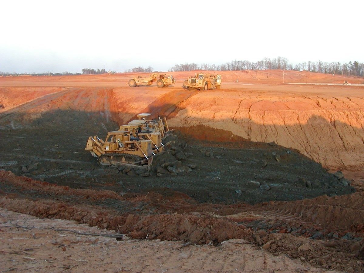 A group of bulldozers are working on a dirt field.