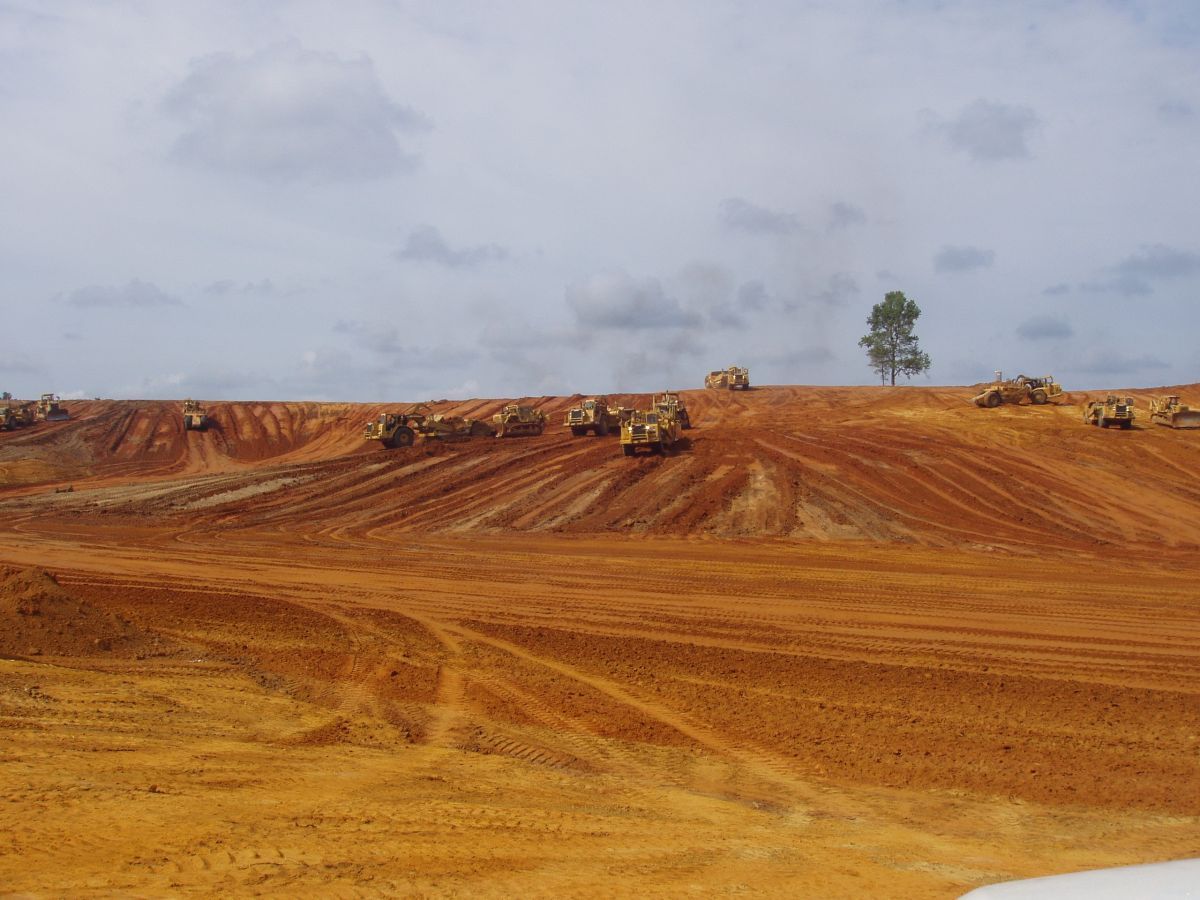 A group of construction vehicles are working on a dirt field.