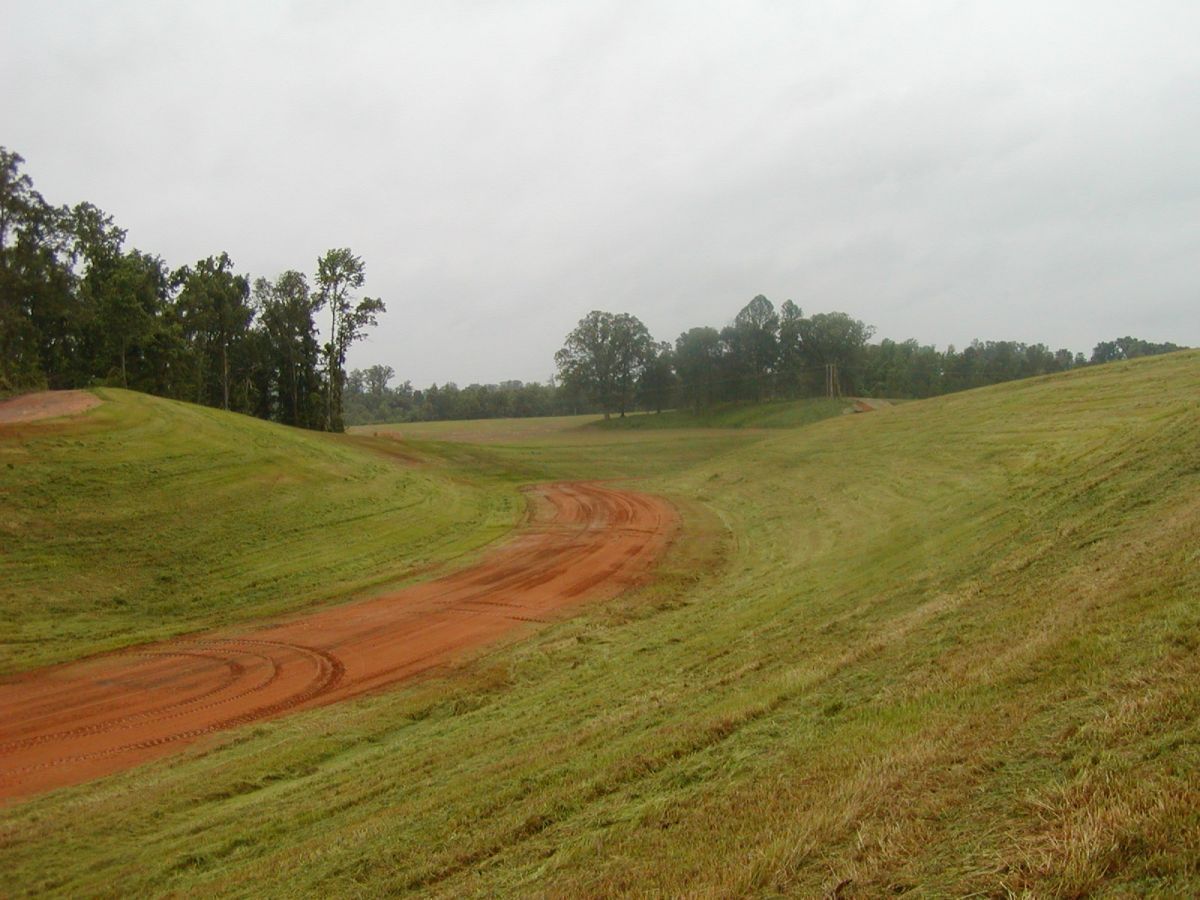 A dirt road going through a grassy field on a cloudy day.