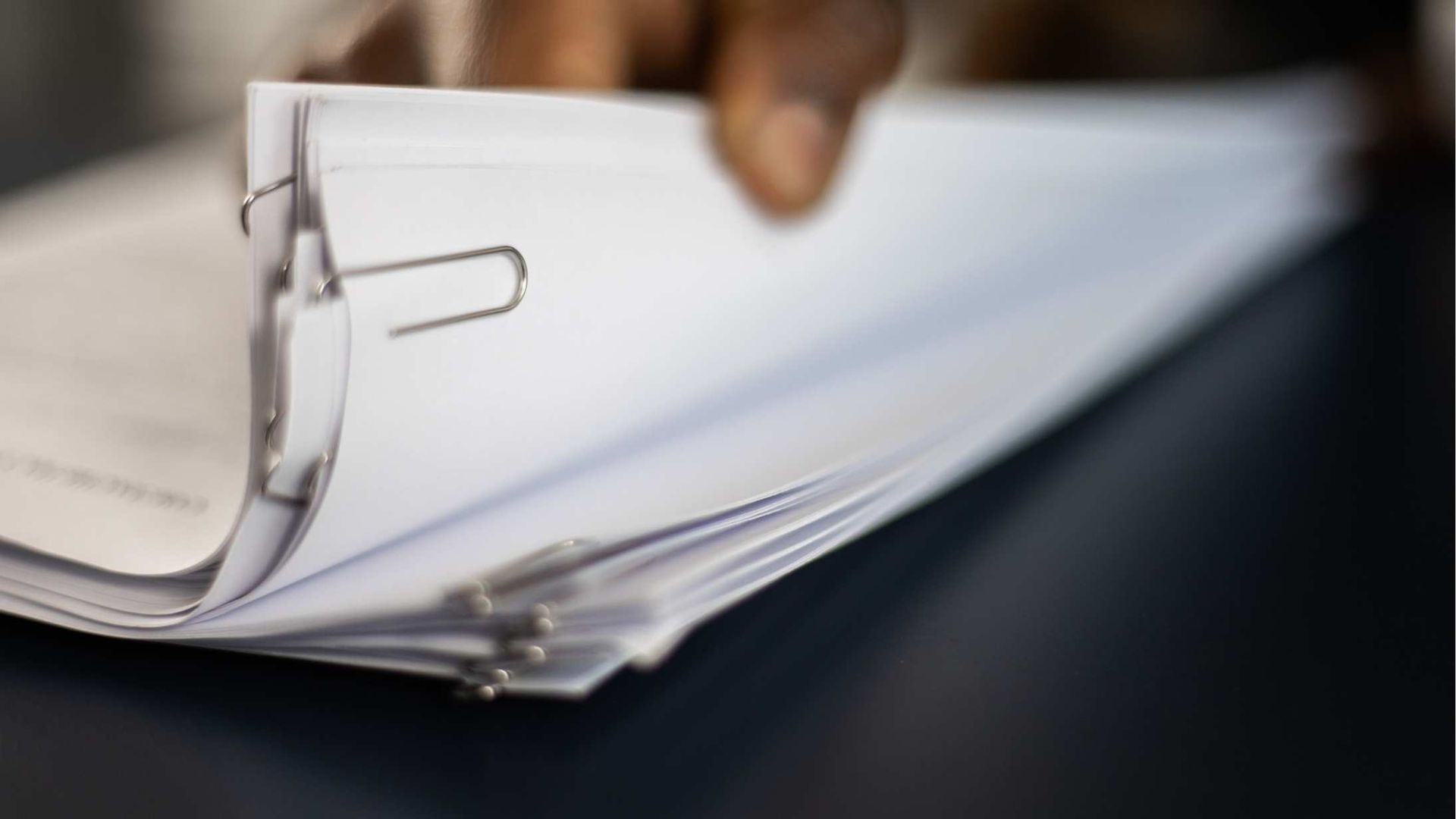 Close-up of a hand flipping through a white binder with metal rings