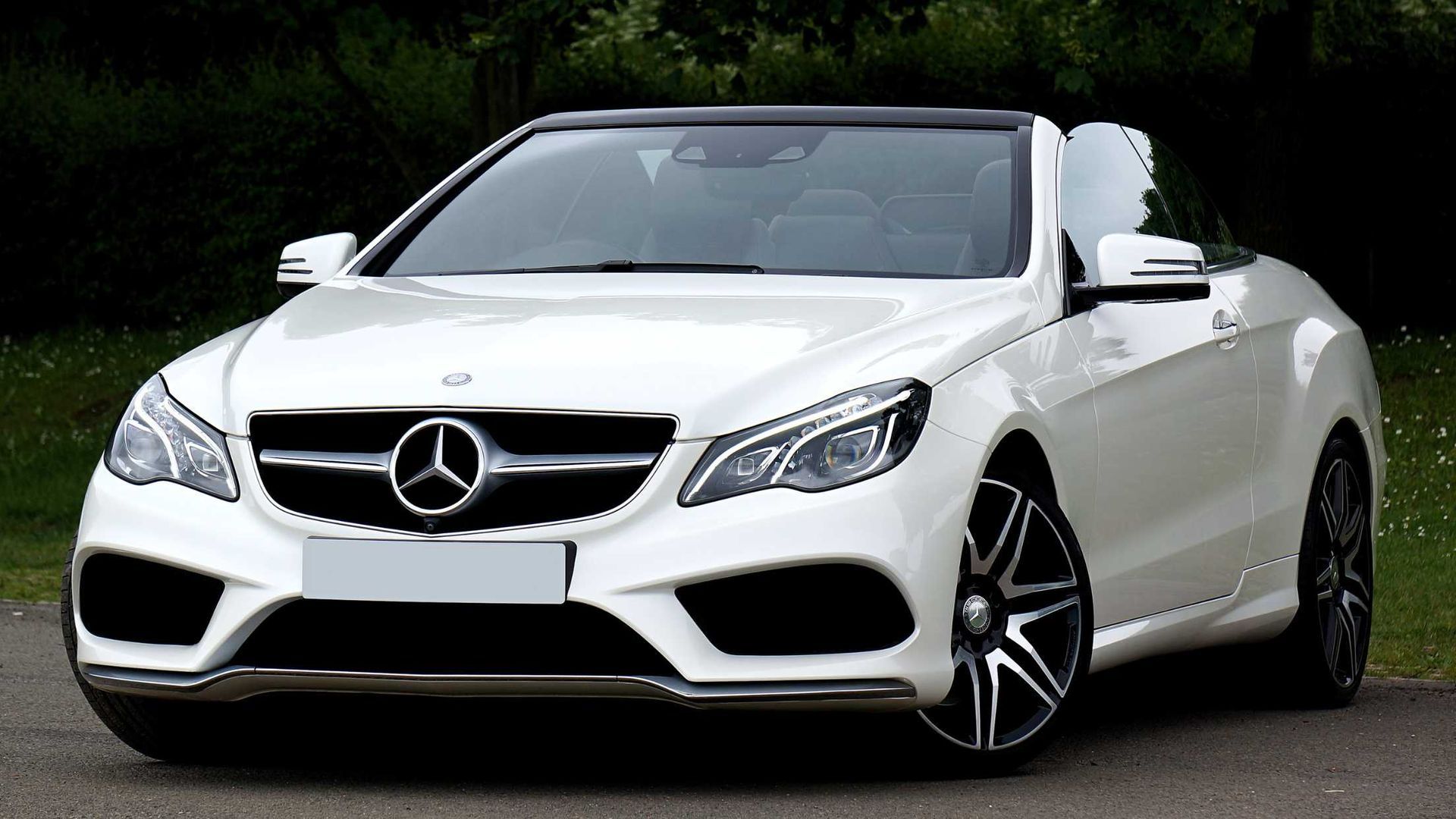 White Mercedes-Benz convertible parked outdoors on a road with trees in the background