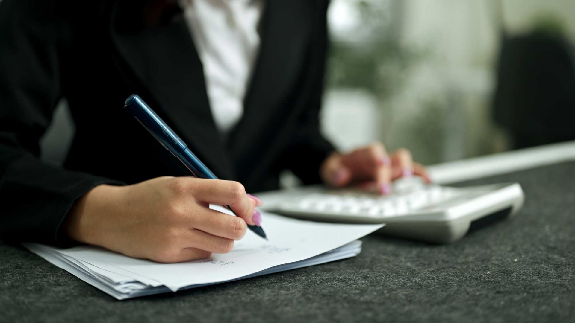 Person writing on paper beside a calculator at a desk