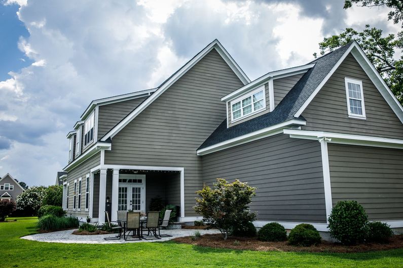 Gray suburban house with white trim, front porch, and manicured lawn under a cloudy sky