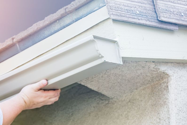 Hand inspecting white roof gutter under the eaves of a house