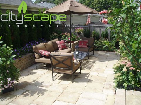 Patio with brick pavers, artificial grass, and wooden planters against a building.