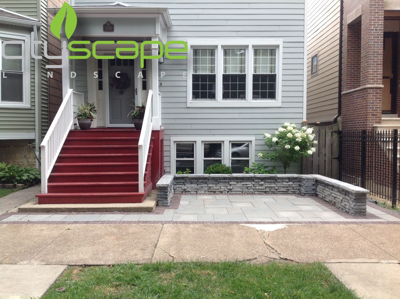A gray house with red steps and a small patio in front. A logo for 