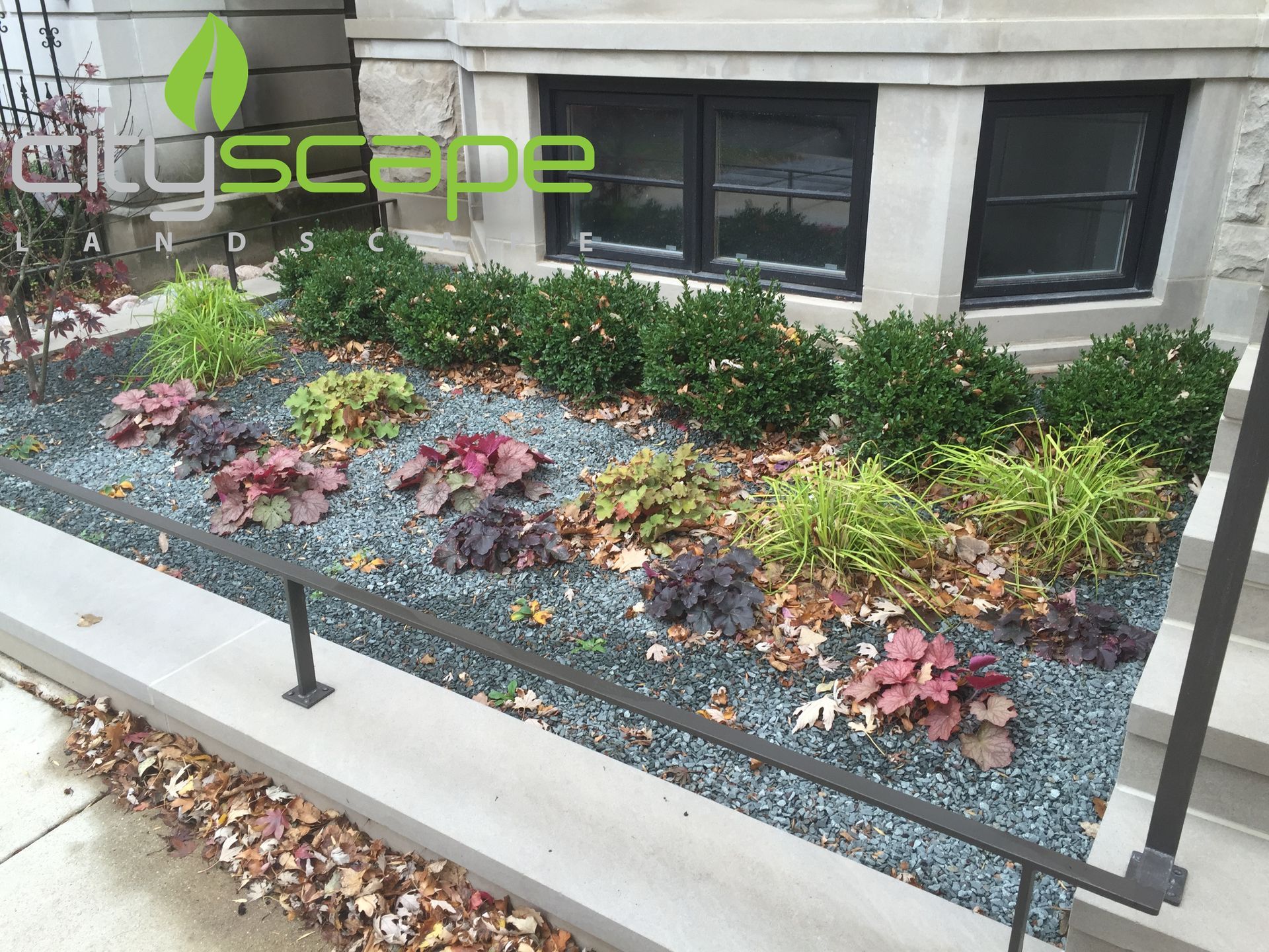 Flowerbed with dark blue gravel, various plants, and a black railing.