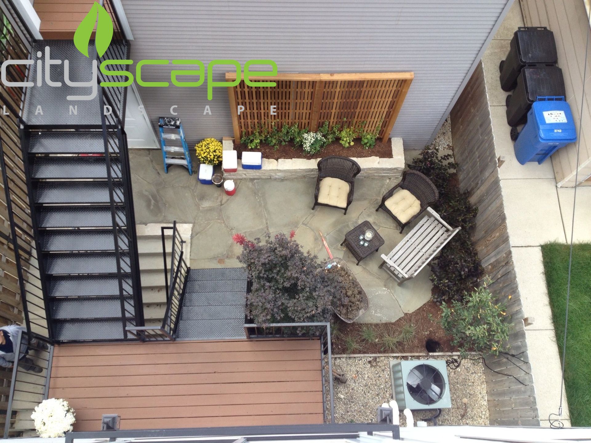 Overhead view of a small backyard patio with seating, garden beds, and an exterior staircase.