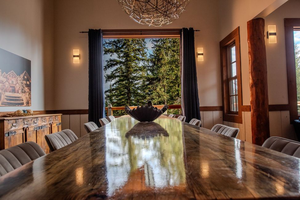 A long wooden table in a dining room with a chandelier hanging from the ceiling.