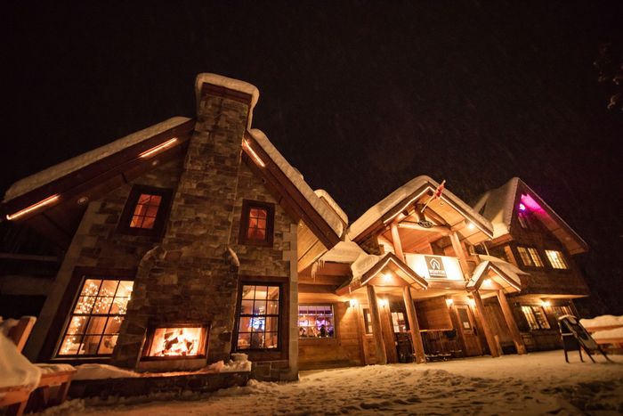 A large house with snow on the roof is lit up at night.