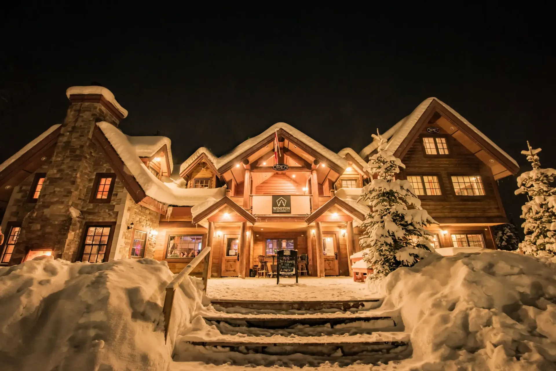 A large wooden house is covered in snow at night.