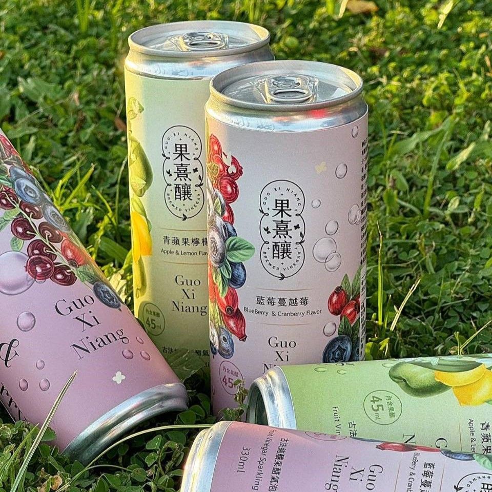 草地上擺放著「果味娘」水果口味汽水罐，罐身上印有水果圖案和中文文字。