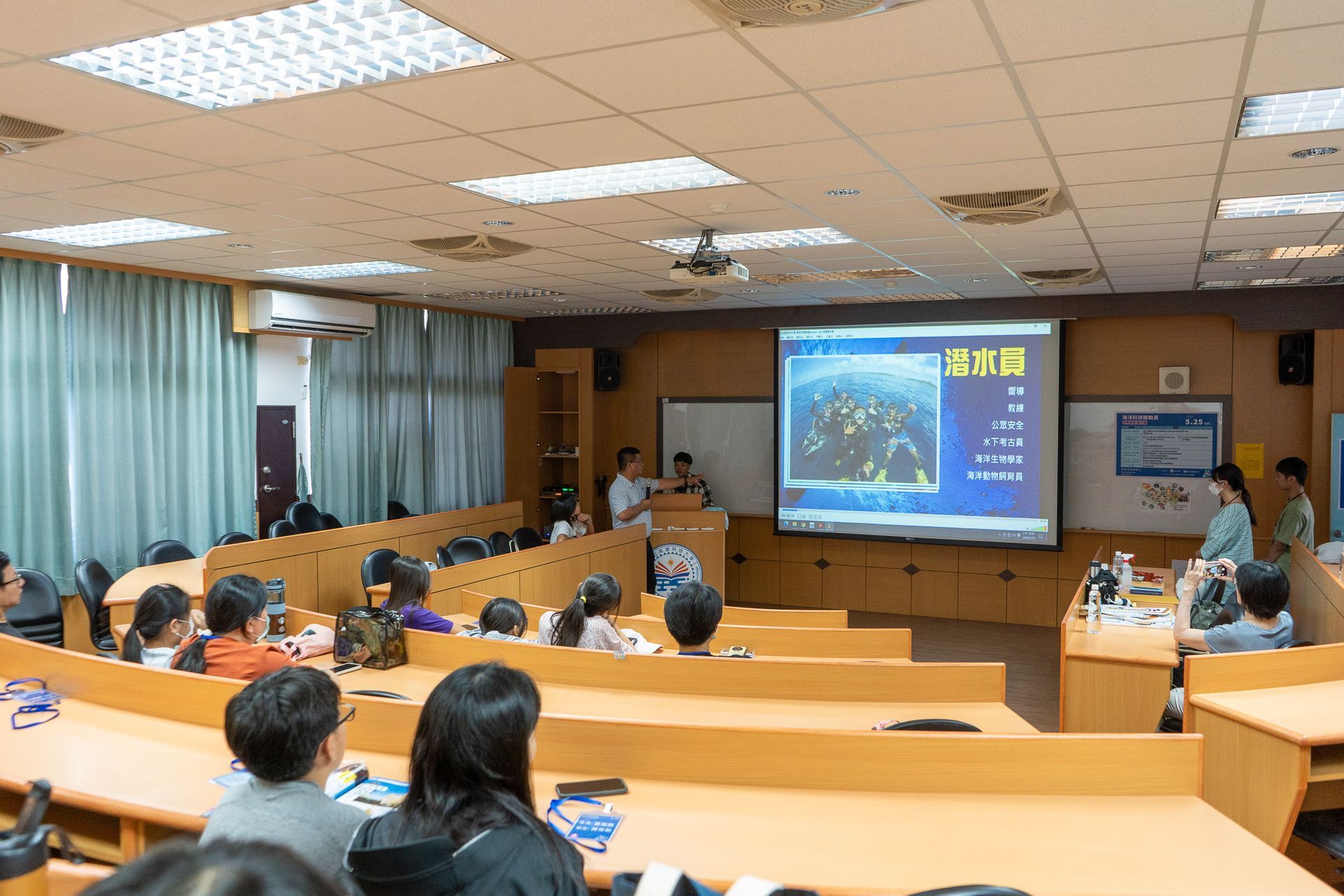 一群人坐在演講廳裡觀看大螢幕上的演示。