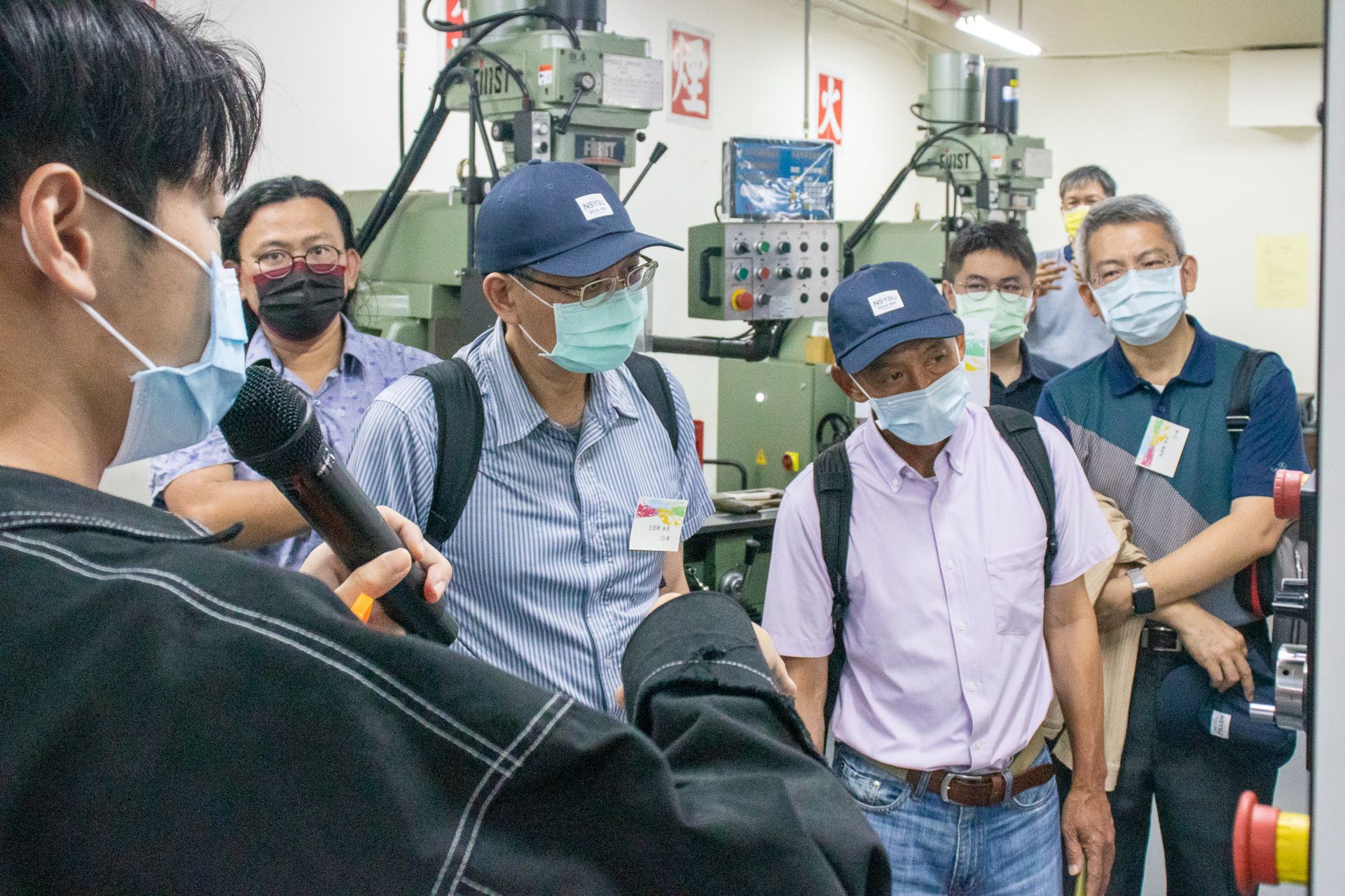 一群戴著口罩的男子站在工廠裡的一台機器周圍。