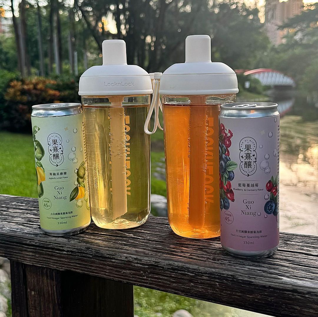 兩杯茶，一杯檸檬味，一杯莓果味，旁邊是帶吸管的水瓶。綠色和紫色的罐子。戶外擺放。
