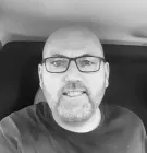 A man with glasses and a beard is smiling in a black and white photo.