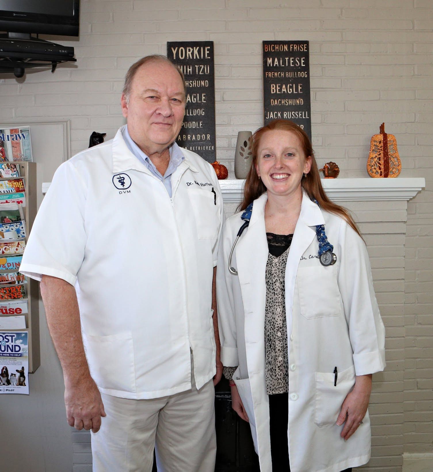 Two people in white coats are smiling indoors in front of a fireplace and menu boards.