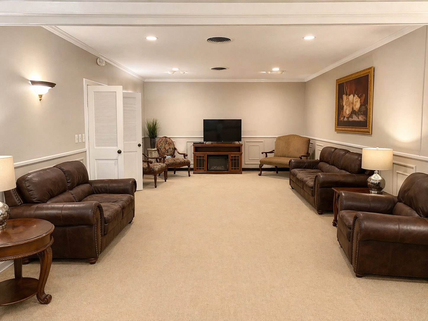 Spacious beige living room with brown leather sofas, lamps, and a TV on a wooden stand.