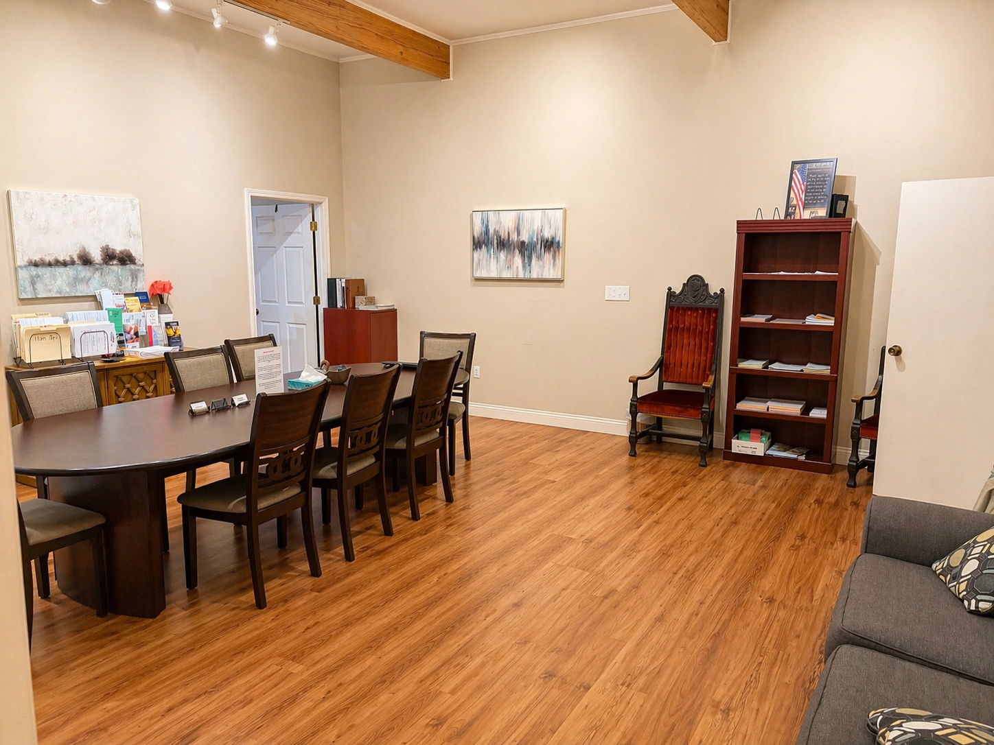 Spacious dining room with wooden table, chairs, shelves, and a gray couch on the right.