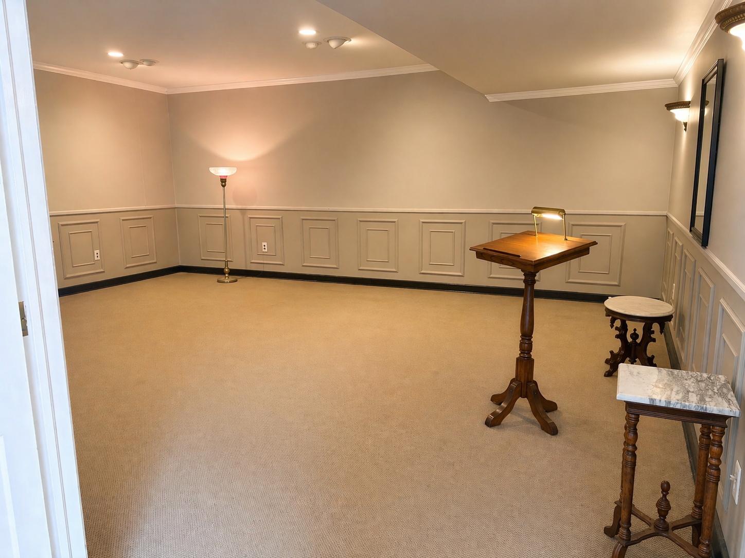 Empty beige carpeted room with paneled walls, lamps, and a small wooden lectern table.