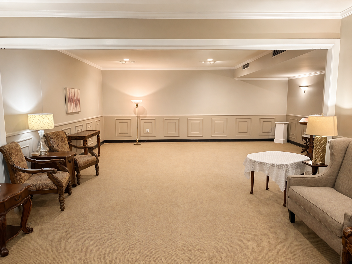 Empty beige hotel lounge with chairs, lamps, and a small round table