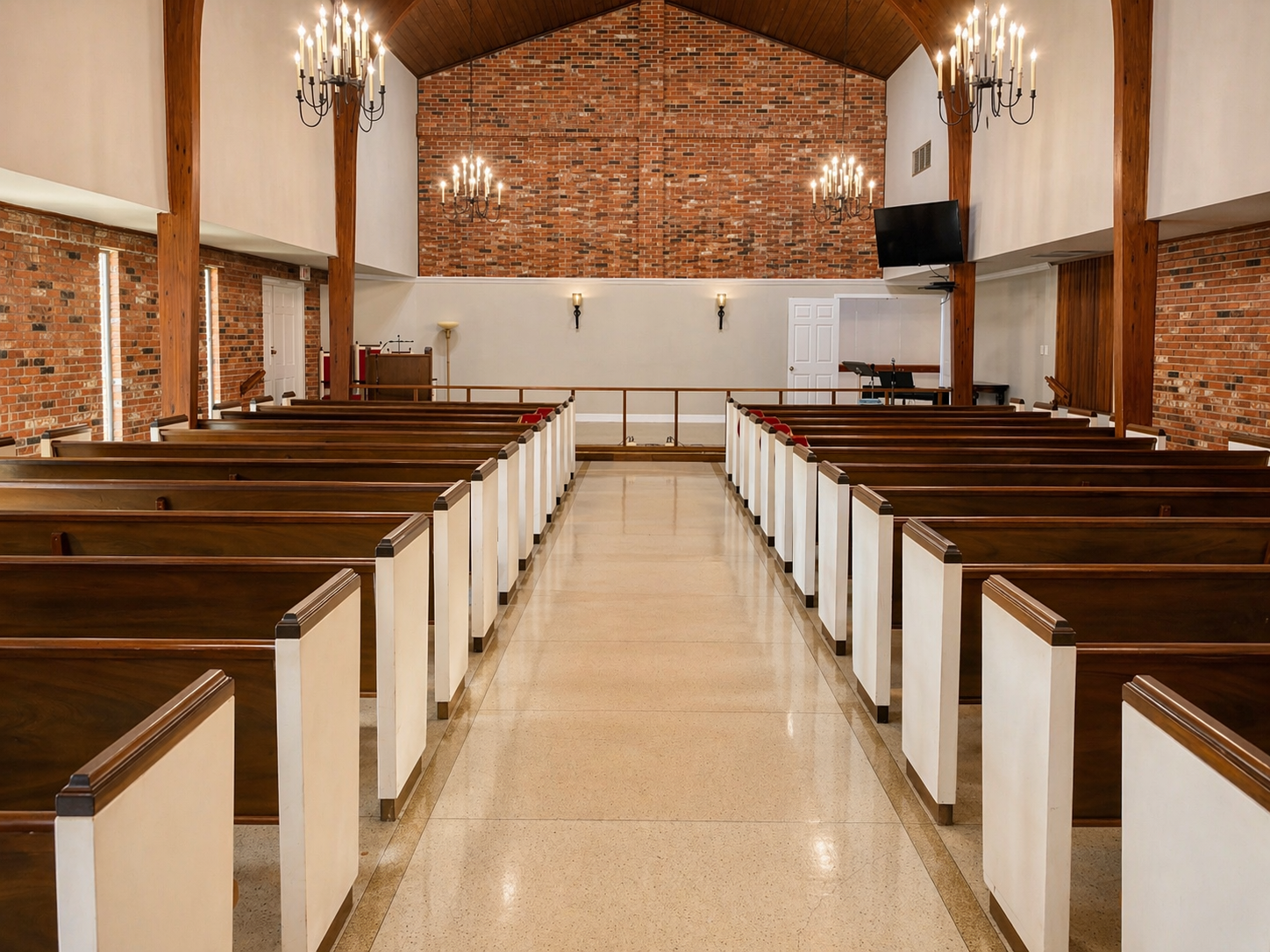 Empty church interior with wooden pews, brick walls, and chandeliers along a central aisle