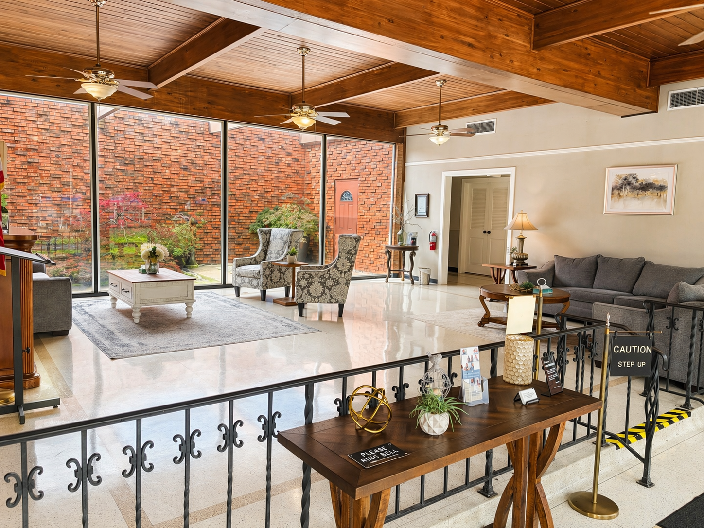 Spacious living room with exposed wood beams, brick wall, gray sofa, and an open patio area.