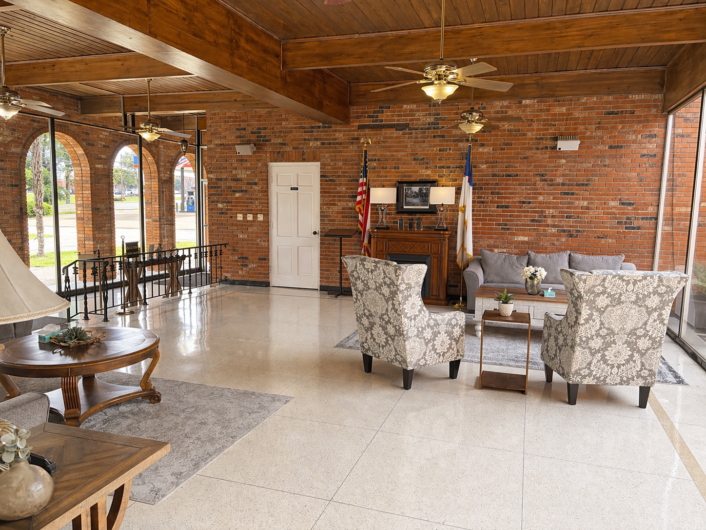 Spacious rustic living room with brick walls, tiled floor, ceiling fan, and upholstered chairs near a fireplace
