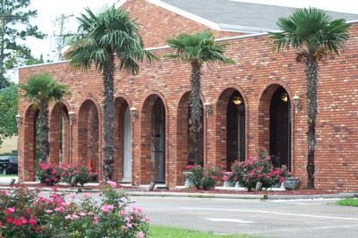 Brick building with arched windows, palm trees, and pink flowers in front