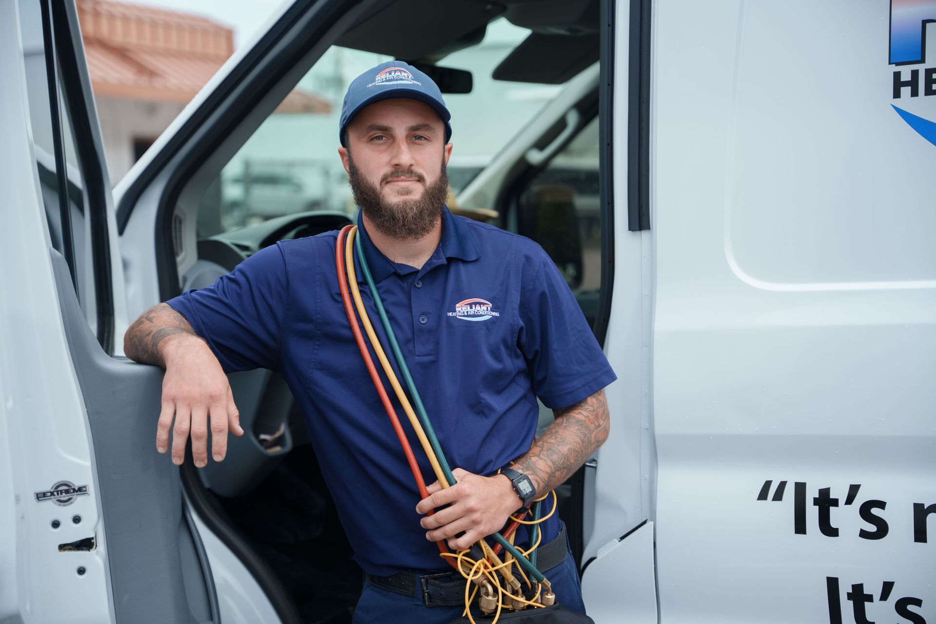 A Reliant Heating & Air Conditioning technician with a beard is leaning on the door of a van.