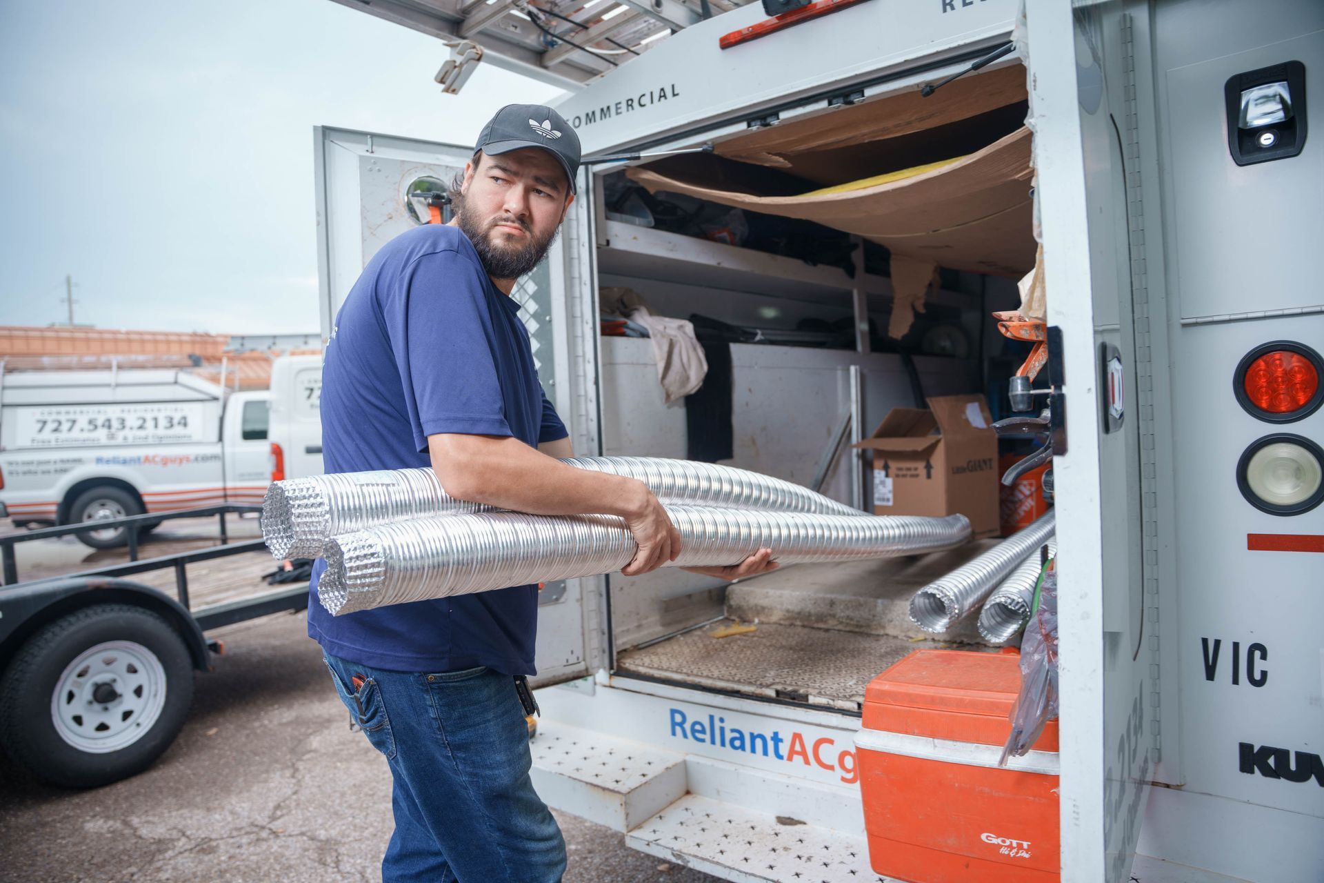 A Reliant Heating & Air Conditioning technician is carrying a bunch of pipes out of a truck.