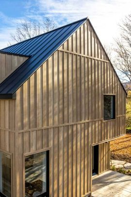 Modern wooden house with a black metal roof and large windows.