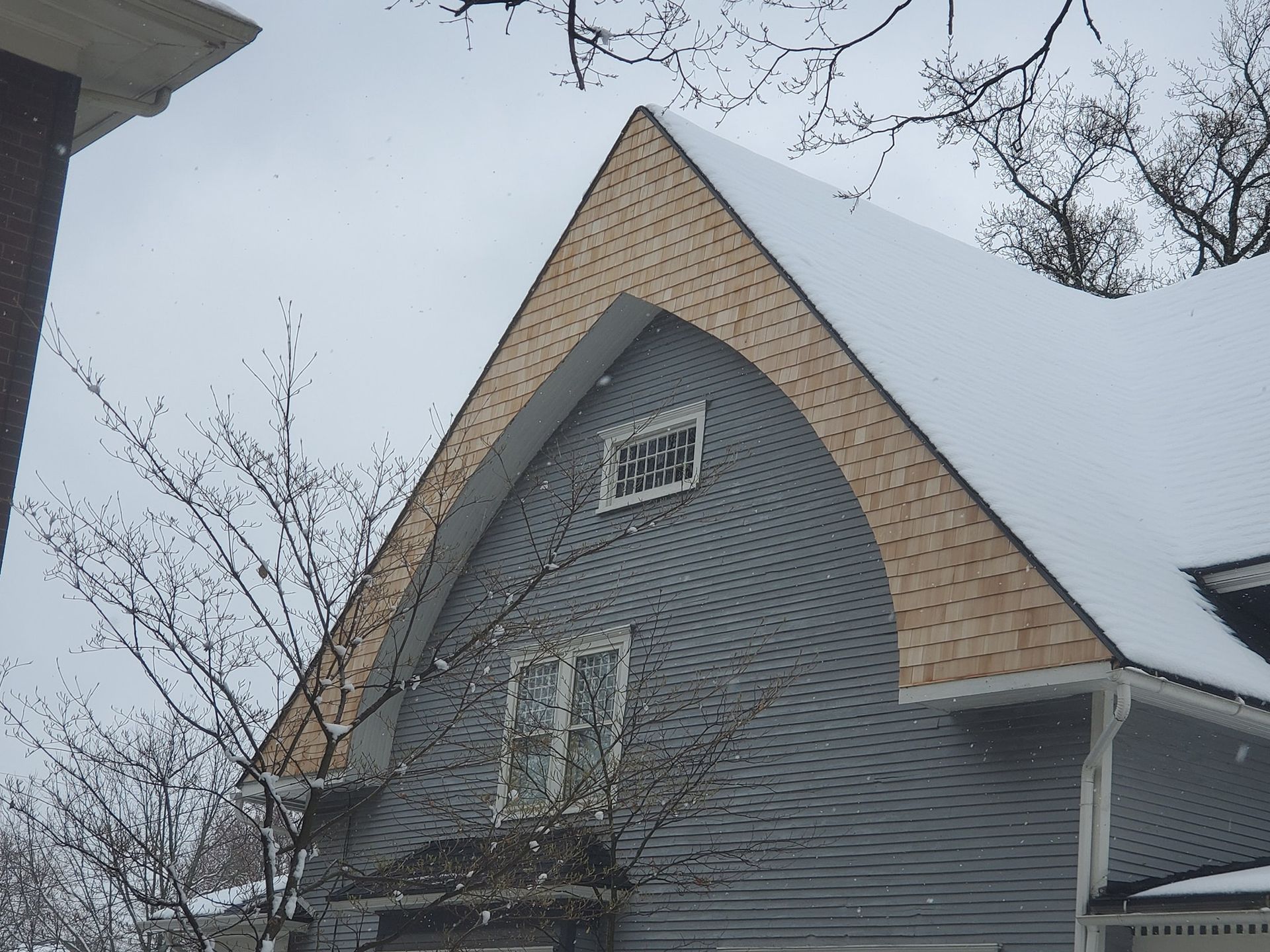 Gray house with a curved roof covered in snow, light-colored trim, and a small window.