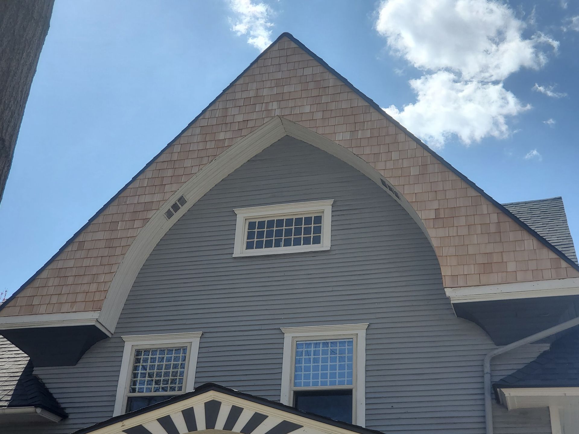 Gray house with a wood-shingled gable, white-framed windows, and blue sky.