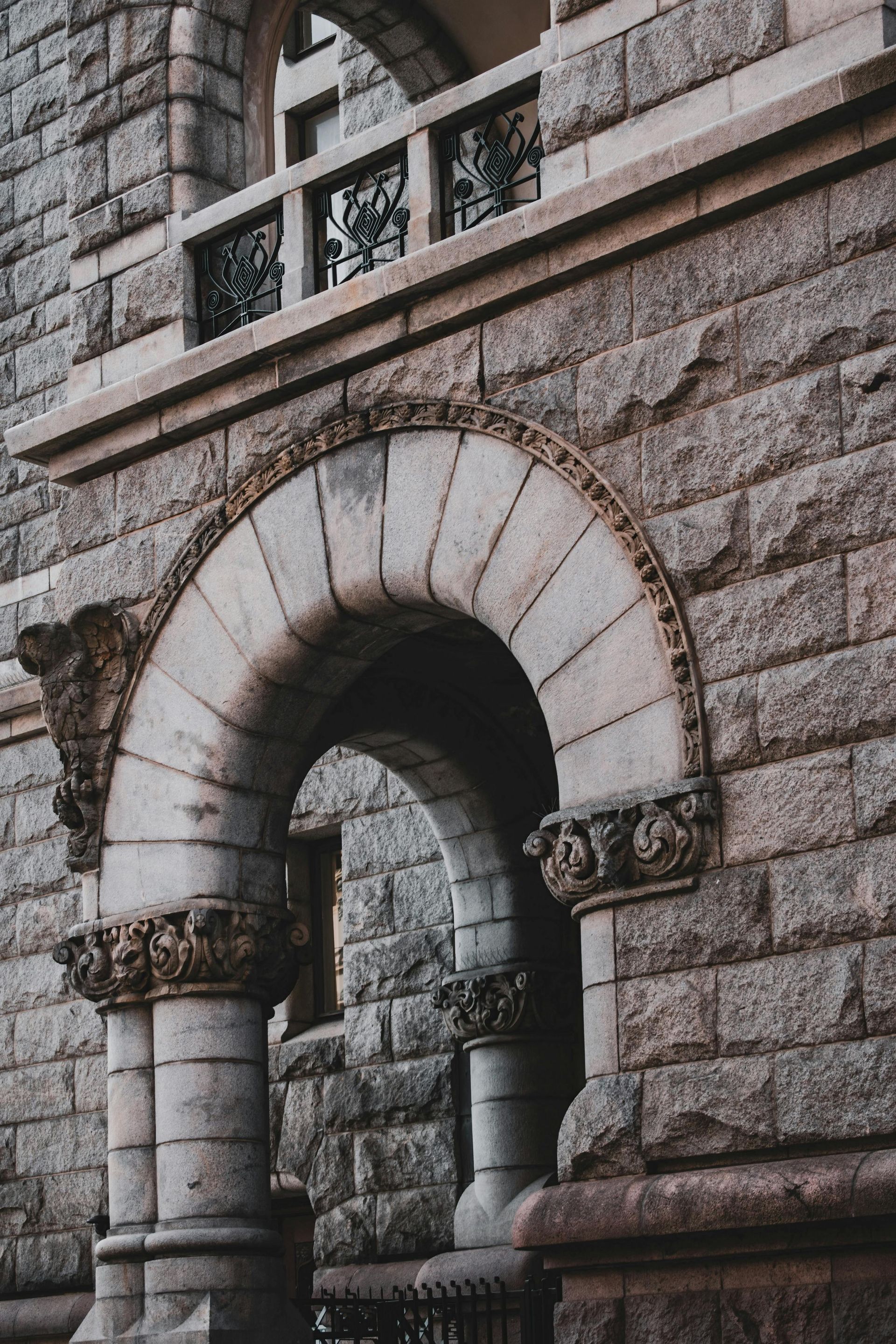 Stone archway entrance to a building with ornate details and a balcony above.