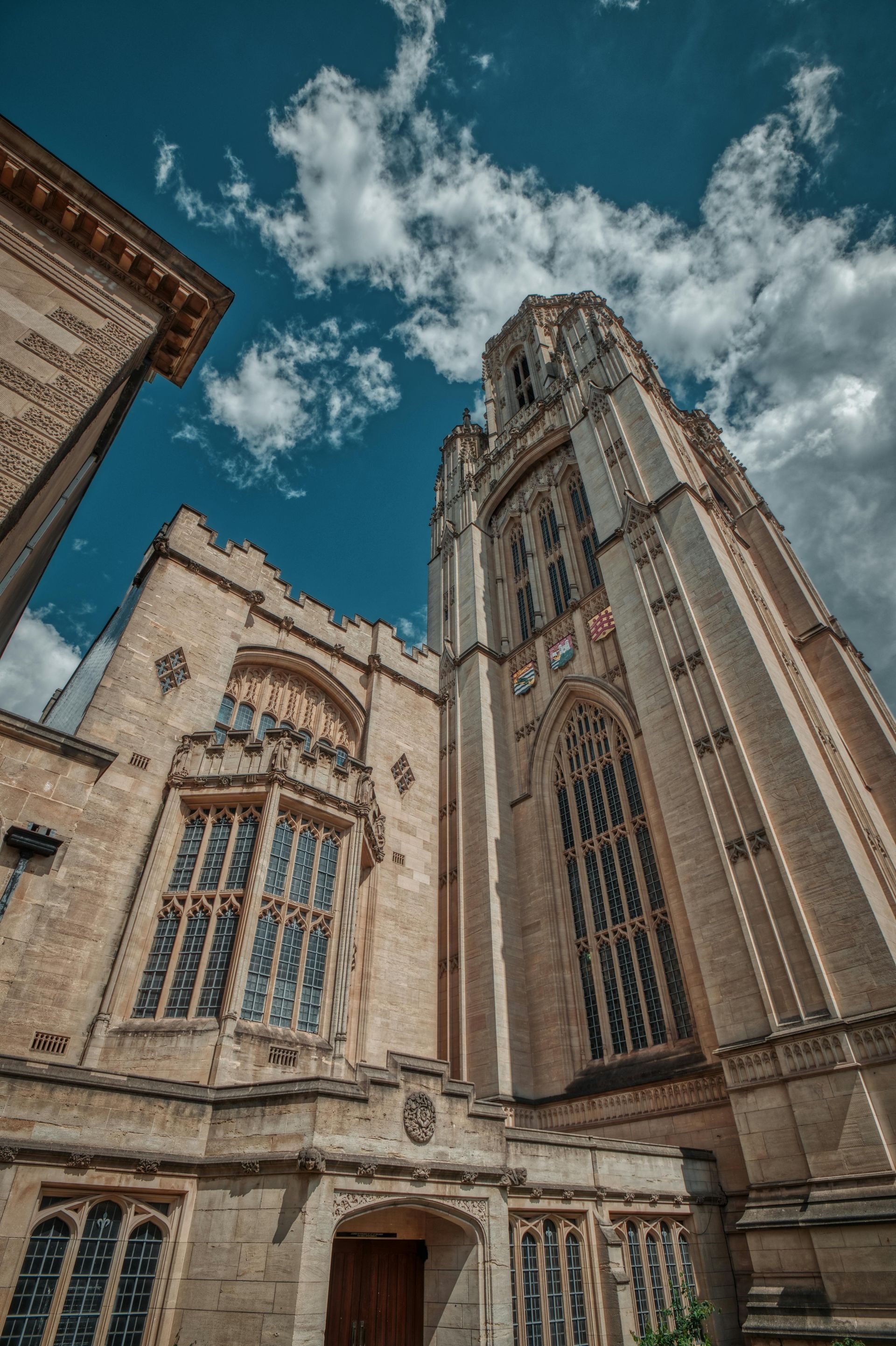 Stone Gothic building with tall tower under a cloudy blue sky.