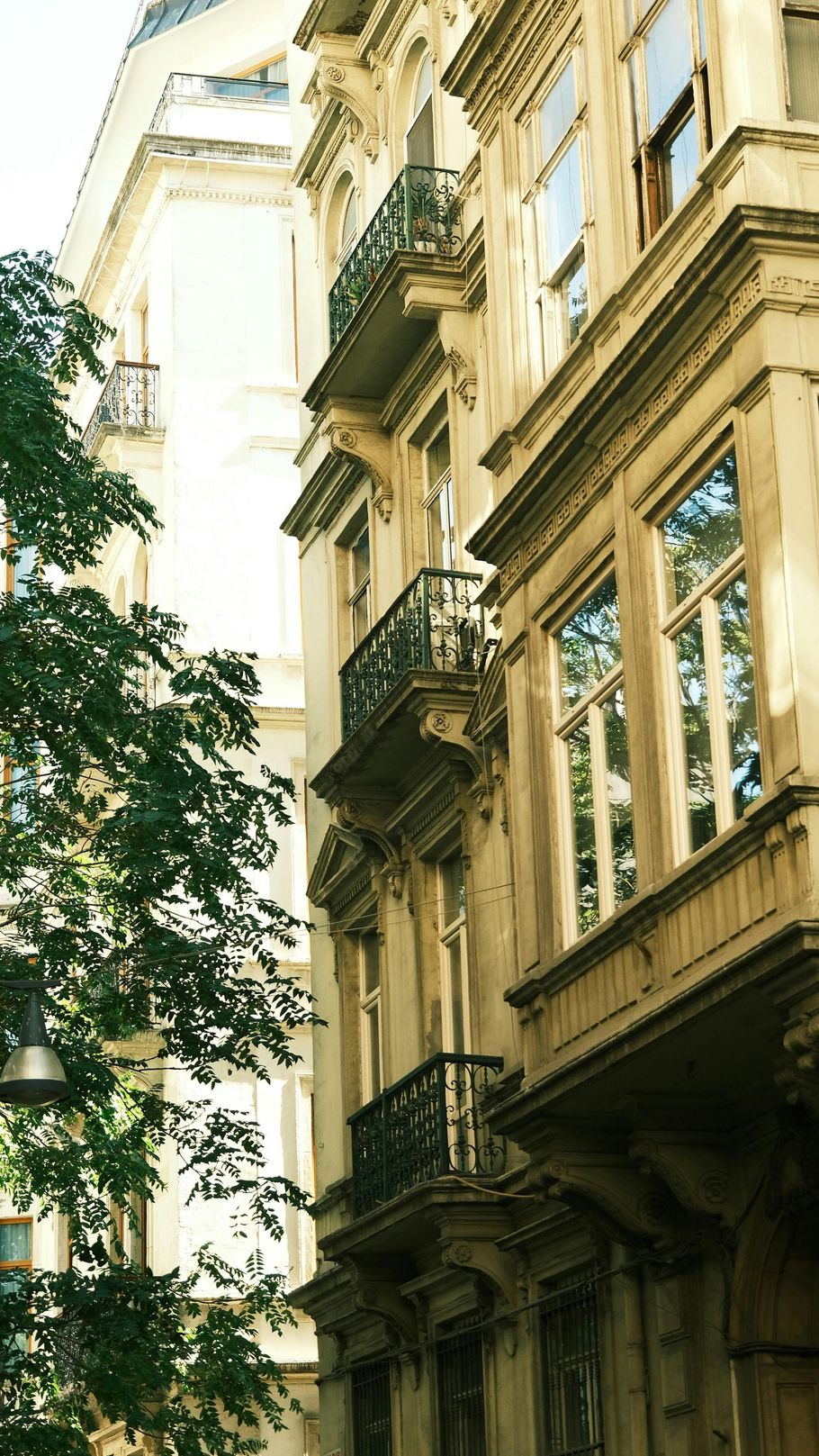 Ornate European building facade with balconies and detailed trim, bathed in sunlight.