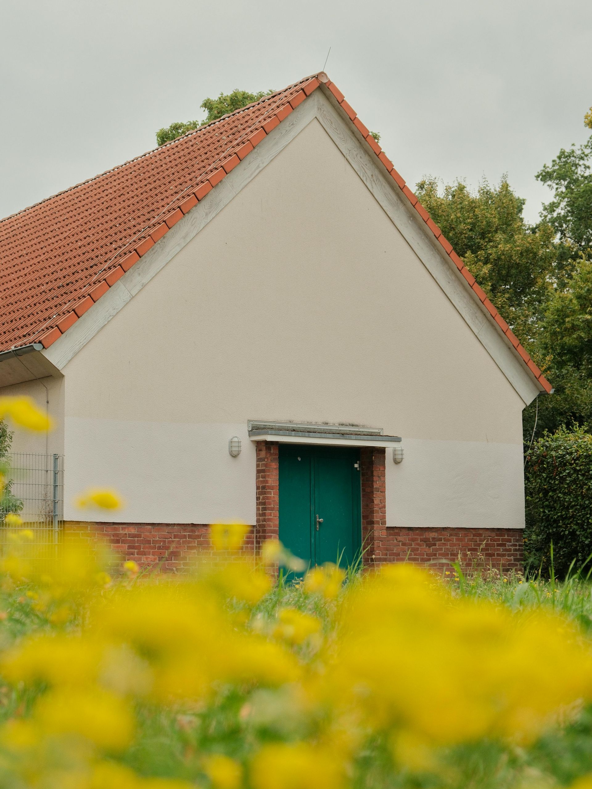 White building with red roof, green door, and yellow flowers in front.