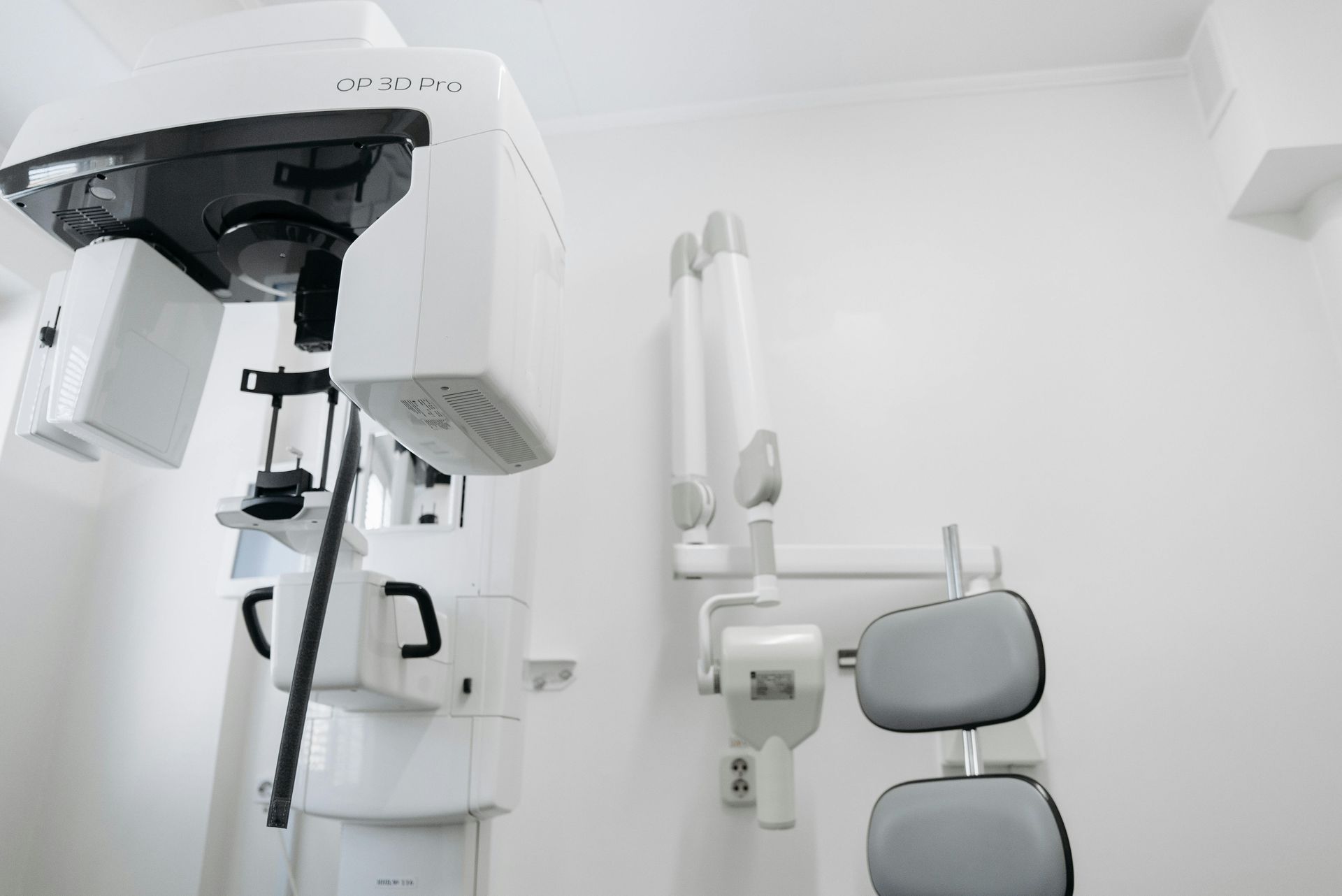 Aparelho de raio-X odontológico e cadeira odontológica contra uma parede branca em uma clínica.