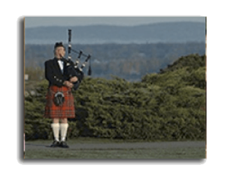 Bagpiper in a red tartan kilt standing outdoors with hills in the background