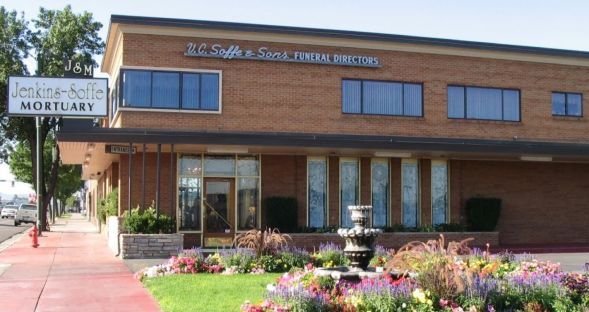 Brick public building with sign, red sidewalk, and flower bed in front.