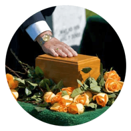 Hand on a wooden coffin surrounded by orange roses at a graveside funeral