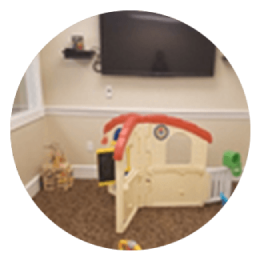 Children’s play area with a red-and-beige playhouse beneath a wall-mounted TV and small toy shelf