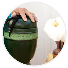 Hand resting on a green decorative urn beside a white flower arrangement
