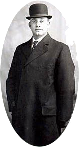Studio portrait of a man in a dark suit and bowler hat, standing against a plain backdrop