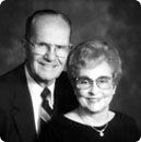 Smiling elderly couple posing closely in a black-and-white portrait.