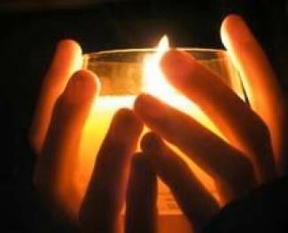 Hands cupping a glowing candle flame in warm, dim light