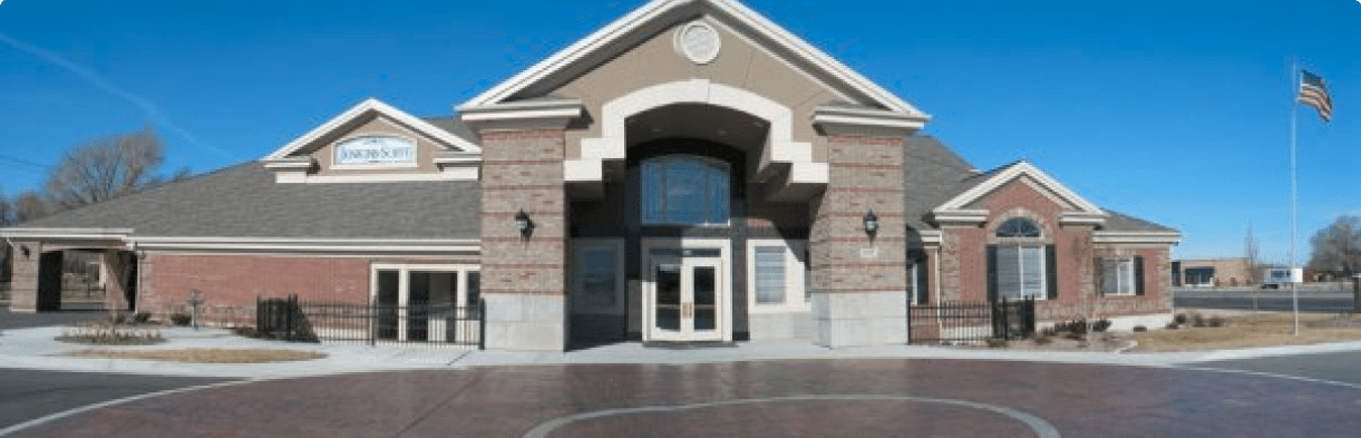 Brick civic building with arched entrance, glass doors, and an American flag in front under a clear blue sky