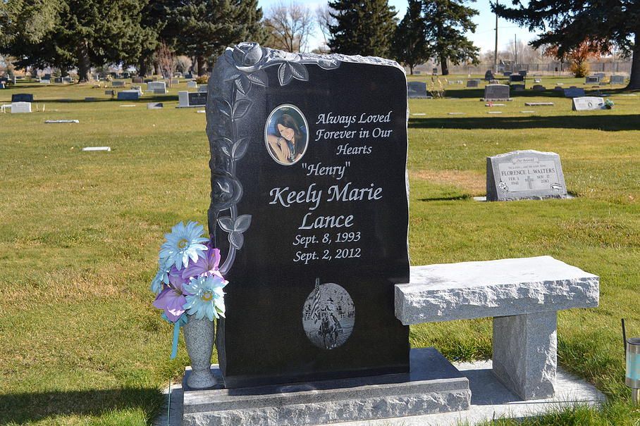 Black gravestone with purple flowers in a sunny cemetery grass plot