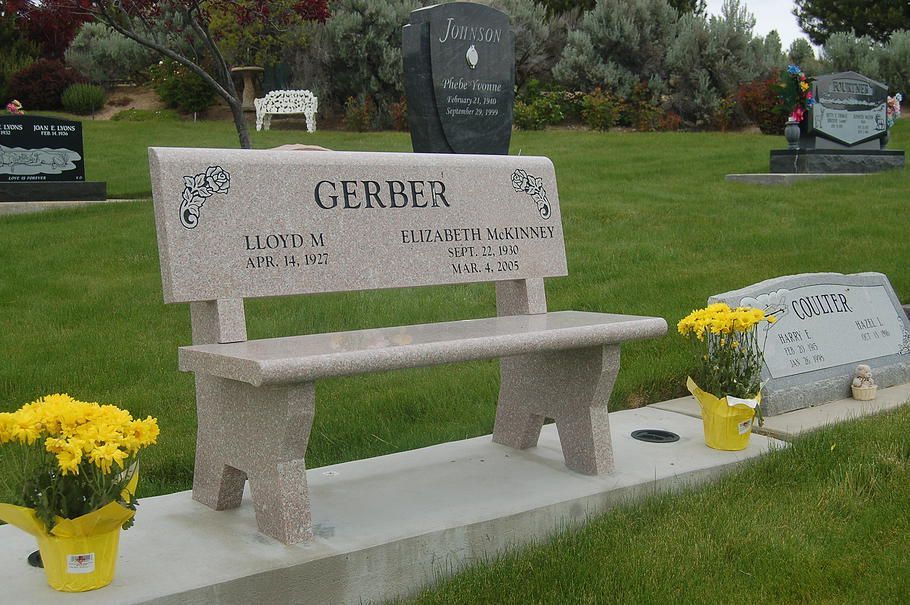 Stone memorial bench grave with yellow flower pots in a cemetery
